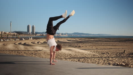 Young-handsome-sporty-man-walking-on-hands-during-workout-on-seaside