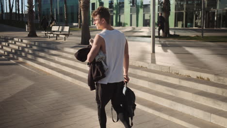 Back-view-shot-of-fit-guy-with-backpack-walking-along-street-after-training-outdoor