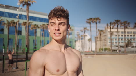 Tracking-shot-of-young-handsome-muscular-man-resting-after-hard-workout-on-beach