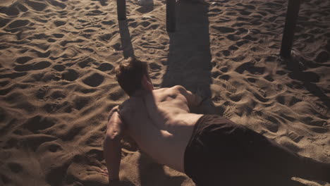 Conceptual-shot-of-young-muscular-man-doing-hard-exercises-during-functional-training-on-sand