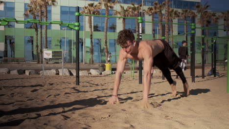 Attractive-fit-guy-doing-exercises-during-functional-training-on-sport-ground-on-beach