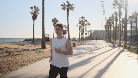 Toma-De-Seguimiento-De-Un-Joven-Deportista-Atractivo-Corriendo-Por-La-Mañana-A-Lo-Largo-De-Una-Hermosa-Playa