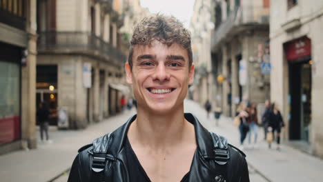 Tracking-out-shot-of-young-handsome-smiling-man-happily-looking-in-camera-on-street