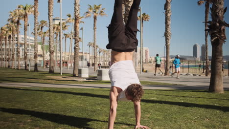 Tracking-out-shot-of-young-sporty-man-standing-on-hands-during-training-outdoor