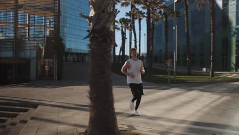 Tracking-shot-of-young-sporty-man-running-in-the-morning-through-city-street