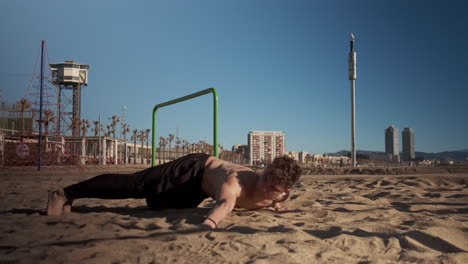 Young-handsome-muscular-man-doing-hard-exercises-during-functional-training-on-beach