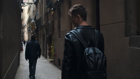 Back-view-shot-of-young-attractive-man-with-backpack-walking-around-narrow-city-street