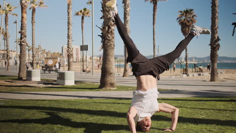 Tracking-shot-of-young-attractive-man-standing-on-head-during-workout-in-city-park