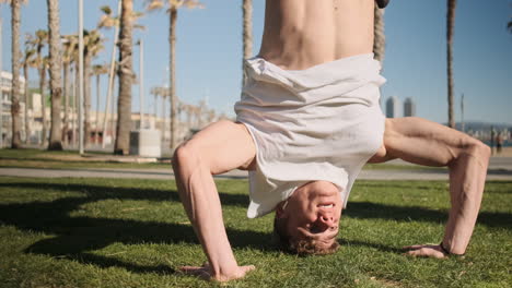 Tracking-out-shot-of-young-sporty-man-standing-on-head-during-training-outdoor