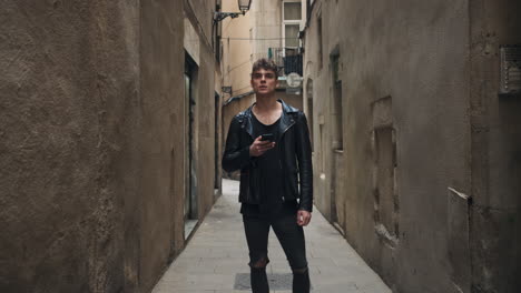 Tracking-in-shot-of-young-attractive-man-with-smartphone-confidently-looking-away-on-narrow-street