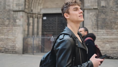 Tracking-shot-of-young-handsome-man-with-smartphone-thoughtfully-looking-around-on-street