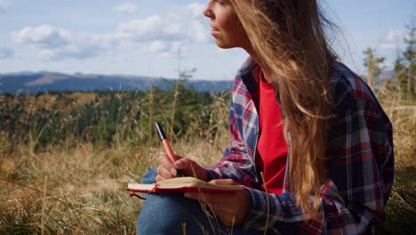 Relaxed-woman-sketching-picture-with-pencil-during-hike-in-mountains