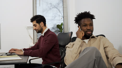 Hombre-Trabajando-En-La-Oficina-Mientras-Su-Amigo-Habla-Por-Teléfono