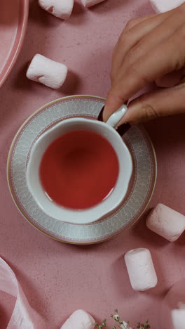 Draufsicht-Auf-Eine-Person,-Die-Eine-Tasse-Tee-Auf-Einem-Rosafarbenen-Tisch-Trinkt