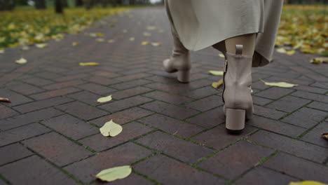 Woman-legs-in-boots-walking-along-path-in-autumn-park