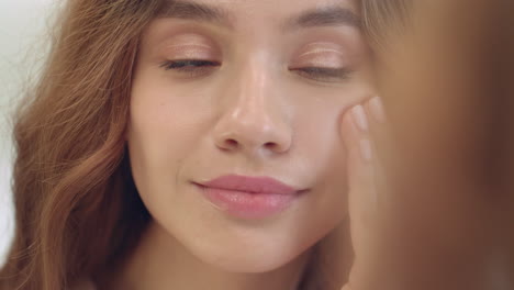 Smiling-woman-applying-moisturizing-cream-on-face-skin