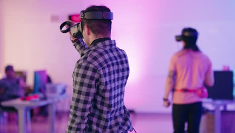 Un-Joven-Afroamericano-Que-Usa-Un-Casco-De-Realidad-Virtual-Se-Da-Vuelta-Dentro-De-Una-Sala-Del-Centro-De-Convenciones-Llena-De-Estaciones-De-Juegos-Vr-Con-Luz-De-Neón-Púrpura