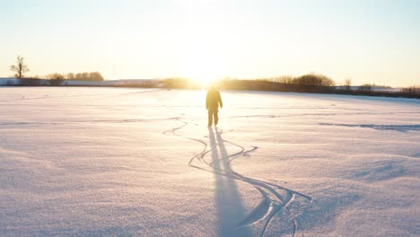 Silhouette-of-person-ice-skate-toward-bright-winter-sunset-on-frozen-lake