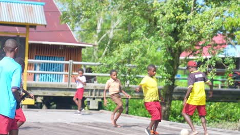 Los-Niños-Papúes-Juegan-Al-Fútbol-En-Un-Campo-Que-Está-Encima-Del-Tablero-En-El-Distrito-De-Asmat-De-Papúa