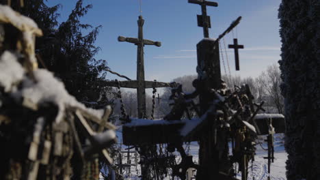 Ancient-Christian-crosses-in-the-middle-of-the-forest-surrounded-by-pines-and-trees,-illuminated-by-the-sun's-rays-in-a-close-up,-under-a-blue-sky,-cinematic-shot-in-slow-motion