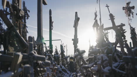 Viele-Kreuze-Angesammelt-Und-Aufgestapelt,-Alte-Religiöse-Kreuze-Mit-Rosenkränzen-Im-Gegenlicht-Mit-Den-Sonnenstrahlen,-Unter-Blauem-Himmel,-Im-Winter,-Filmische-Aufnahme-In-Zeitlupe