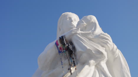 Wonderful-white-statue-of-the-Virgin-Mary-carrying-Jesus-in-her-arms-with-a-beautiful-blue-sky-in-the-background-on-the-Hill-of-Crosses