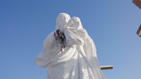 Wonderful-white-statue-of-the-Virgin-Mary-carrying-Jesus-in-her-arms-with-a-beautiful-blue-sky-in-the-background-on-the-Hill-of-Crosses