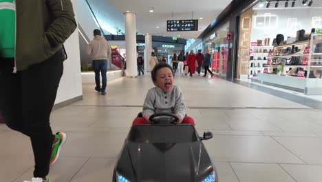 Feliz-Niño-Negro-De-3-Años-Conduciendo-Un-Coche-De-Juguete-Negro-Eléctrico-Dentro-De-Un-Centro-Comercial