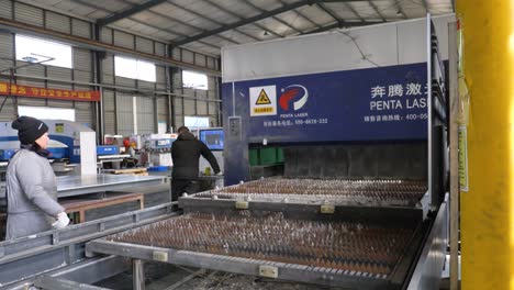 Hand-held-shot-of-metal-spikes-entering-and-exiting-heavy-machinery-with-workers-in-a-Chinese-factory