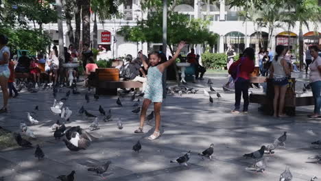 Niña-Persigue-Palomas-En-La-Concurrida-Plaza-De-La-Ciudad-De-Santa-Cruz,-Bolivia