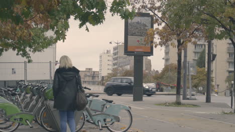 Blonde-Frau-Läuft-An-Stadtfahrrädern-Vorbei,-Die-Auf-Einer-Straße-Geparkt-Sind