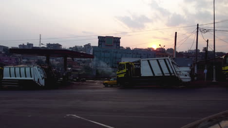 Camiones-De-Basura-En-Una-Gasolinera-En-El-Centro-De-Yaundé,-Puesta-De-Sol-En-Camerún,-África