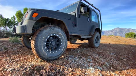 Cool-black-Jeep-4x4-car-on-a-sunny-day-on-La-Quinta-mountain-top-with-green-trees-and-blue-sky,-fun-ATV-adventures-in-Marbella-Malaga-Spain,-4K-shot