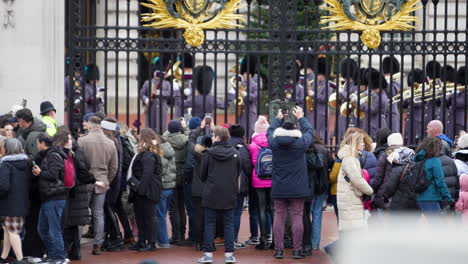 Turistas-Tomando-Fotografías-Con-Teléfonos-En-La-Puerta-Del-Palacio-De-Buckingham-Mientras-La-Banda-De-Guardia-Del-Rey-Toca-Canciones,-Ceremonia-De-Cambio-De-Guardia