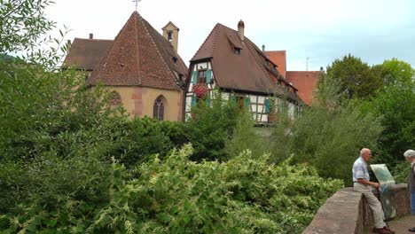 Older-Couple-Rests-Near-Bridge-in-Kayserberg-Village