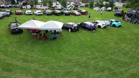 Toma-Aérea-De-Una-Exhibición-De-Autos-Al-Aire-Libre-Y-Un-Evento-Con-Carpas-En-El-Parque-De-Verano