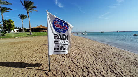 Die-Flagge-Des-Fünf-Sterne-Tauchresorts-Padi-Weht-Im-Wind-An-Einem-Strand-Im-Sonnigen-Dahab,-Ägypten