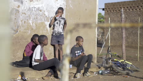 Vier-Kleine-Jungen-Sitzen-Vor-Einem-Spaza-Laden-Im-Township,-Trinken-Coca-Cola-Und-Unterhalten-Sich