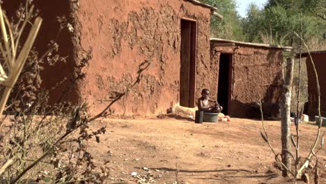 Un-Joven-Africano-Usa-Una-Tina-De-Plástico-Para-Bañarse-Afuera-De-Su-Tradicional-Casa-De-Barro