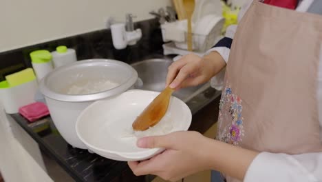 Person-Wearing-Apron-Scooping-Steamed-Rice-From-The-Cooker