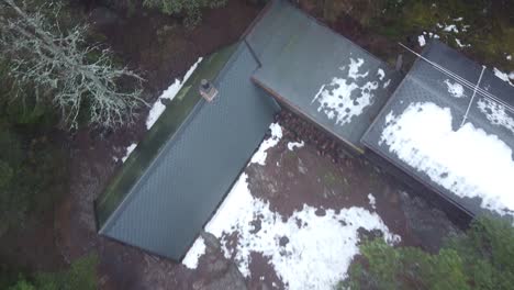 Aerial-view-ascending-above-an-a-frame-cabin-or-lodge-in-a-thick-forest-into-the-fog-above