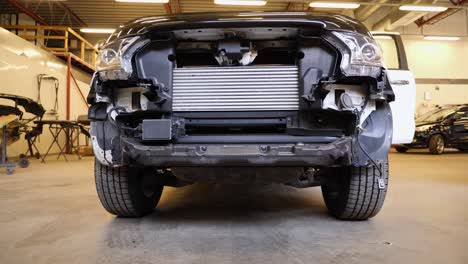 Sliding-or-trucking-view-of-the-stripped-down-front-end-of-a-damaged-SUV-in-the-garage-for-repairs