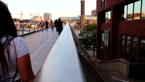 Young-woman-with-backpack-crossing-busy-Millennium-Bridge-during-golden-hour-in-London