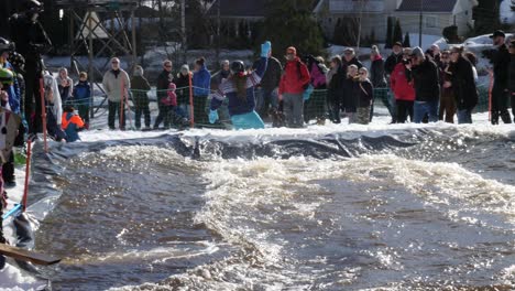 Man-snowboards-down-the-hill-and-across-a-pool-of-water-in-a-community-winter-event-in-slow-motion-showing-good-balance