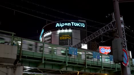 A-train-glides-across-an-elevated-rail-in-the-Shinjuku-district-of-Japan,-unveiling-the-nocturnal-charm-of-the-cityscape