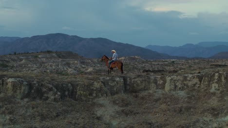 Majestuoso-Vaquero-A-Caballo-En-La-Cresta-De-La-Montaña-Del-Desierto-Al-Atardecer,-Aéreo