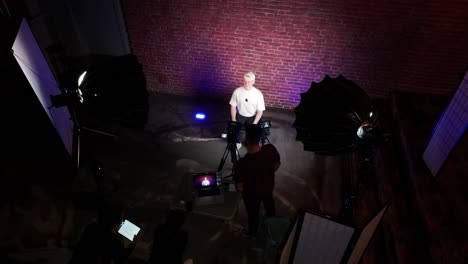 Guy-in-indoor-podcast-studio,-illuminated-red-brick-wall-in-background