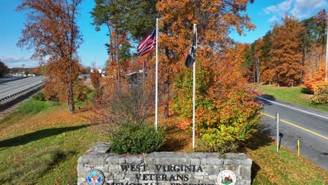 Cartel-De-Piedra-De-La-Autopista-En-Memoria-De-Los-Veteranos-De-Virginia-Occidental-Con-Banderas-Americanas-Y-De-Pow-Mia-Contra-Un-Colorido-Fondo-De-Follaje-De-Otoño