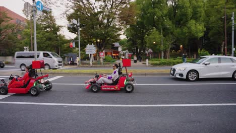 Go-Karts-Fahren-An-Der-Tokyo-Minato-Ward-Street-Vorbei-Und-Winken-Den-Fußgängern-Am-Frühen-Abend-Zu