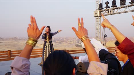 A-singer-performs-on-a-stage-in-front-of-audience-overlooking-pyramids,-Giza-in-Egypt-Arc-shot